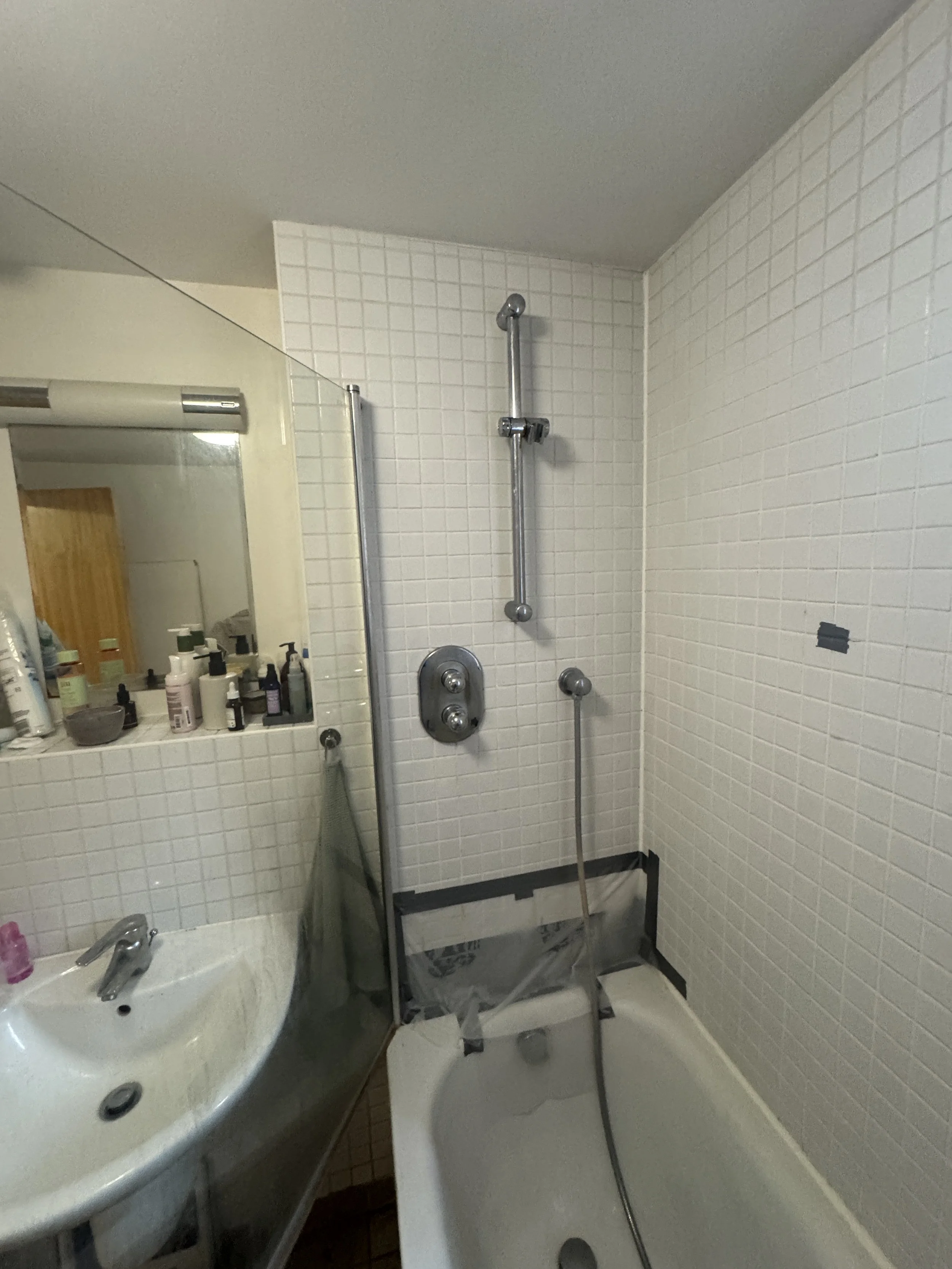 Bathroom with a shower chair, grab bars, a small white bathtub, a sink with toiletries, and a mirror.