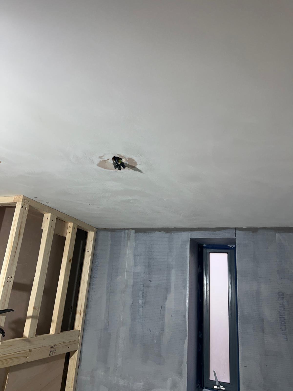 Interior of a room under construction with a partially installed ceiling, a window, and wooden framing for drywall or other wall material.