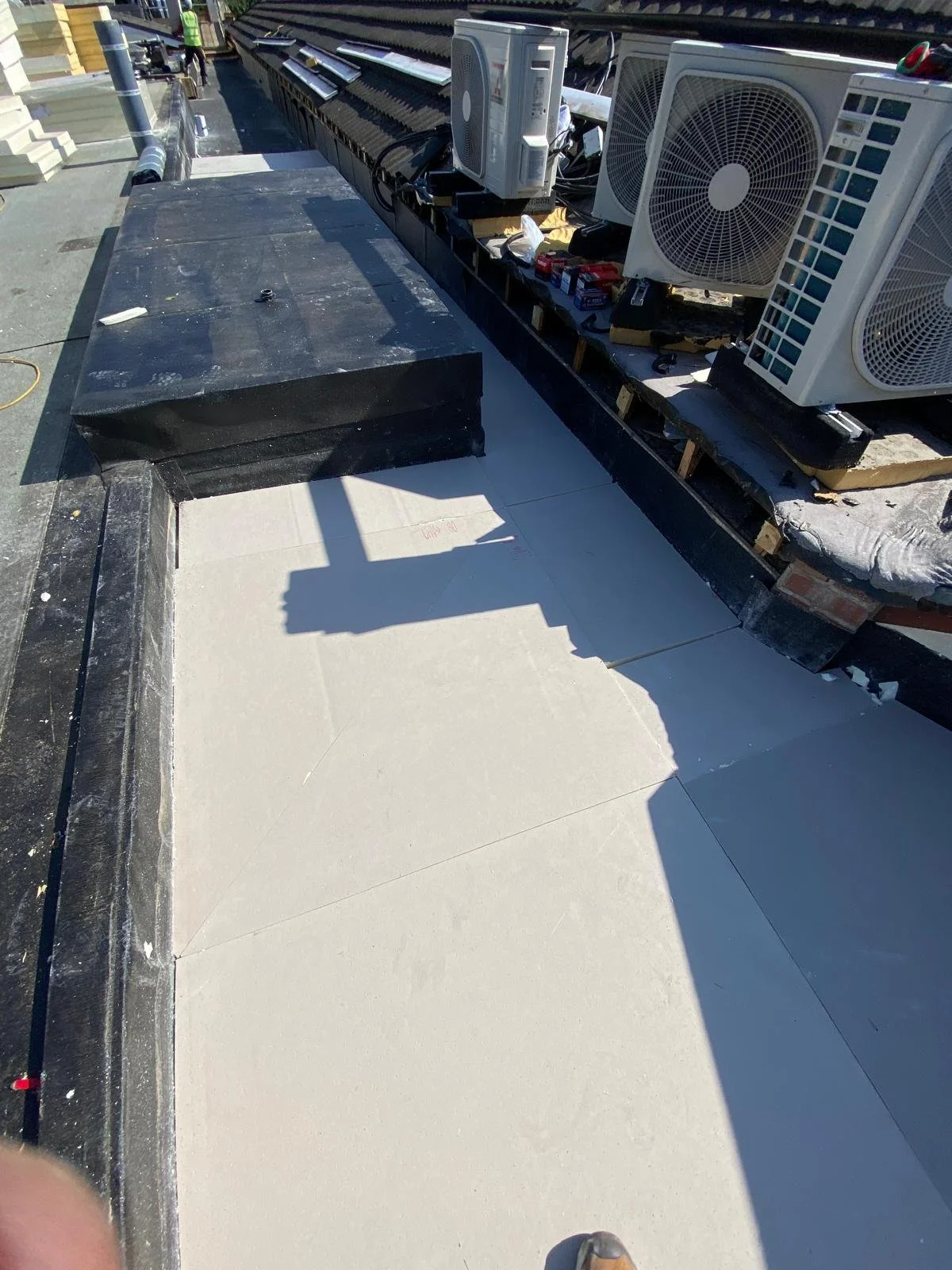 Construction site rooftop with HVAC units, insulation, and building materials, including air conditioning units on the edge of a building roof.