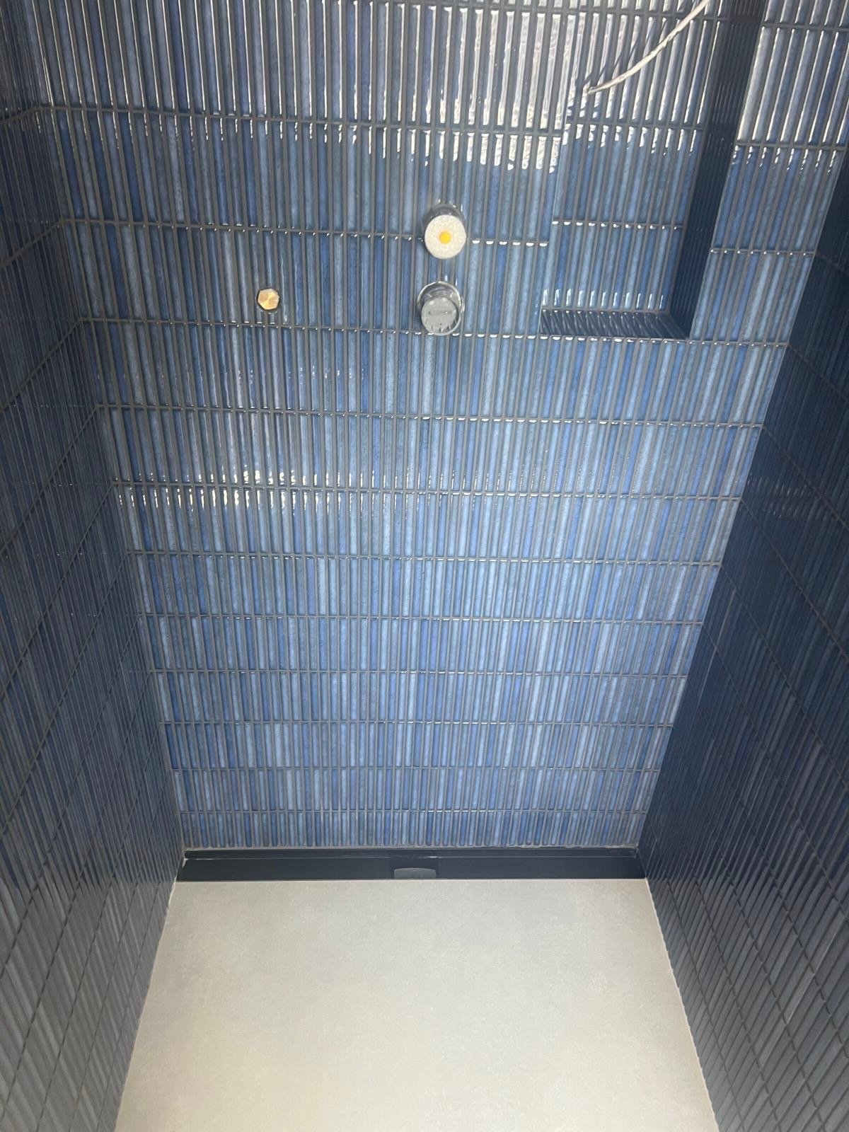 View of an elevator ceiling with a blue tiled wall, electrical fixtures, and a small square window.