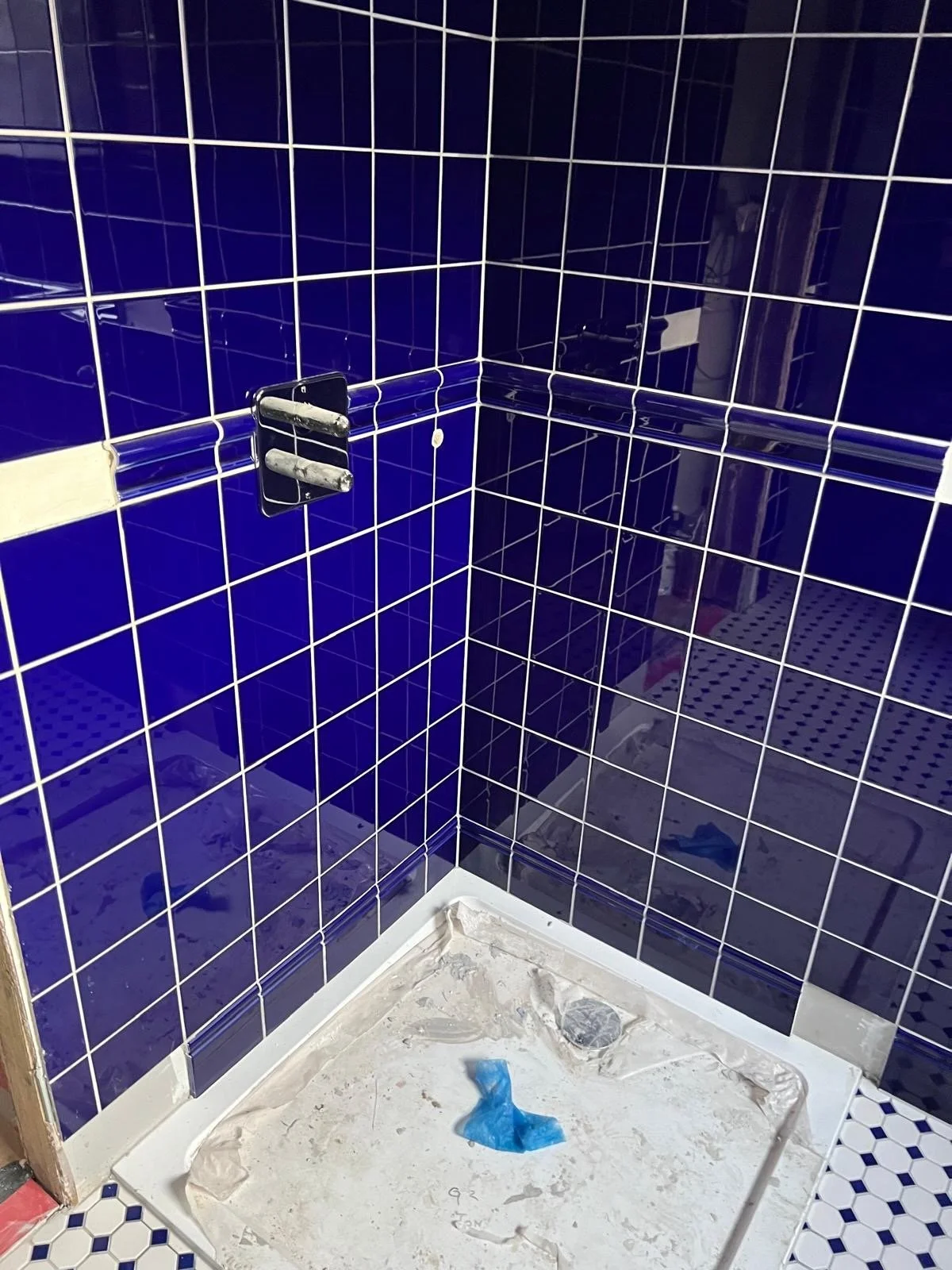 Bathroom corner with blue tiled walls, no fixtures installed, construction debris on the floor.
