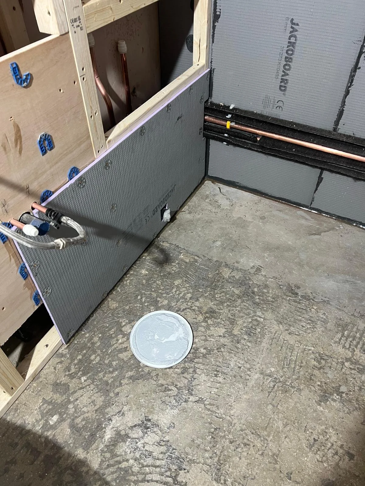 Construction site with plumbing and insulation materials, unfinished wooden framing, and a concrete floor.
