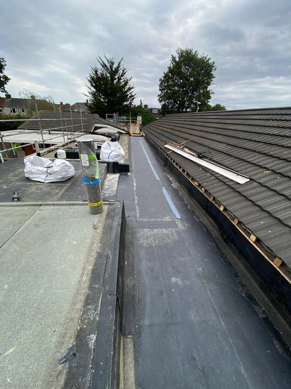View of a rooftop under construction or repair, with roofing materials, tools, and scaffolding, under an overcast sky.
