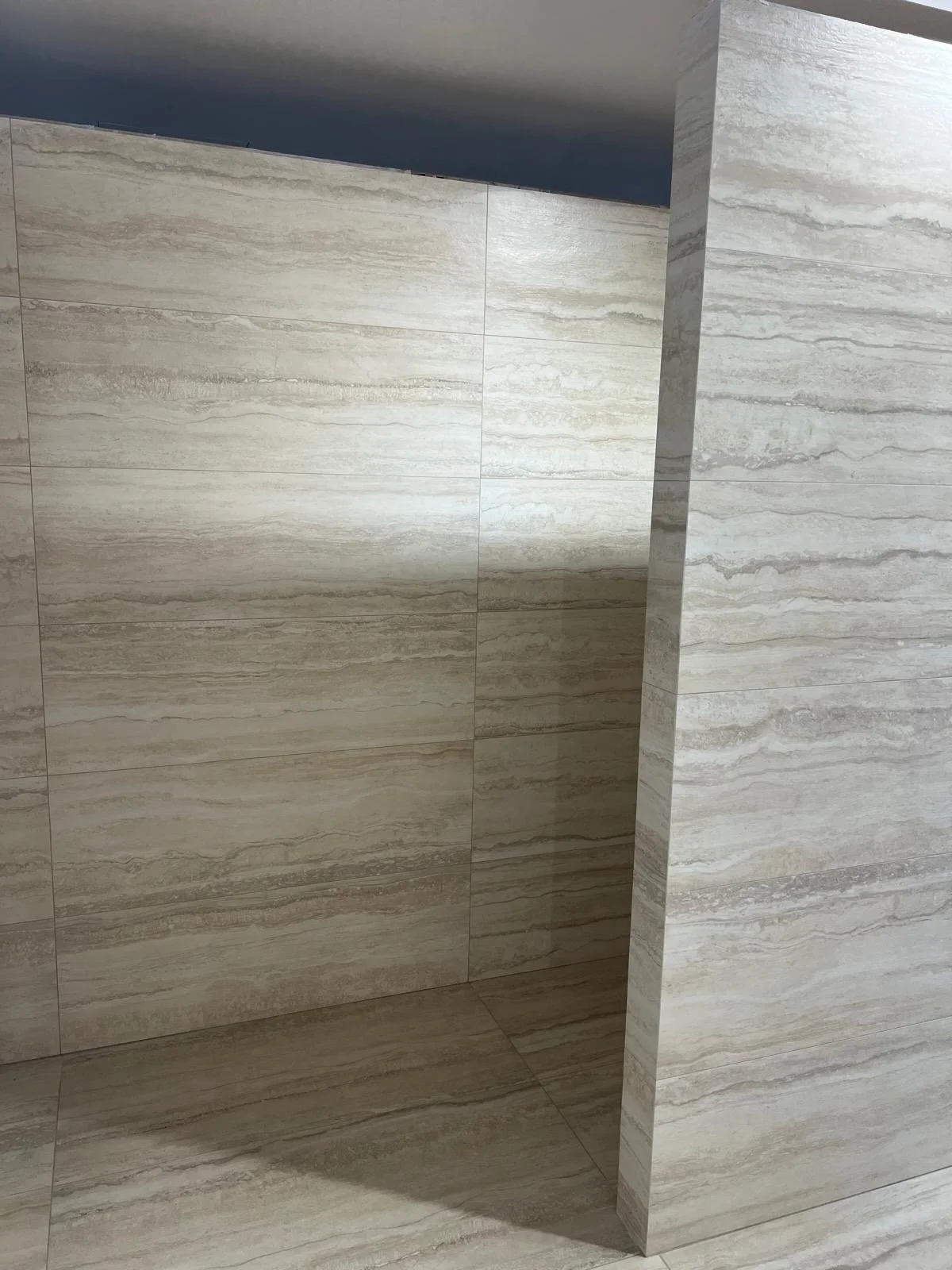 Image showing a corner of a beige marble or stone wall with horizontal striations, in an interior space.