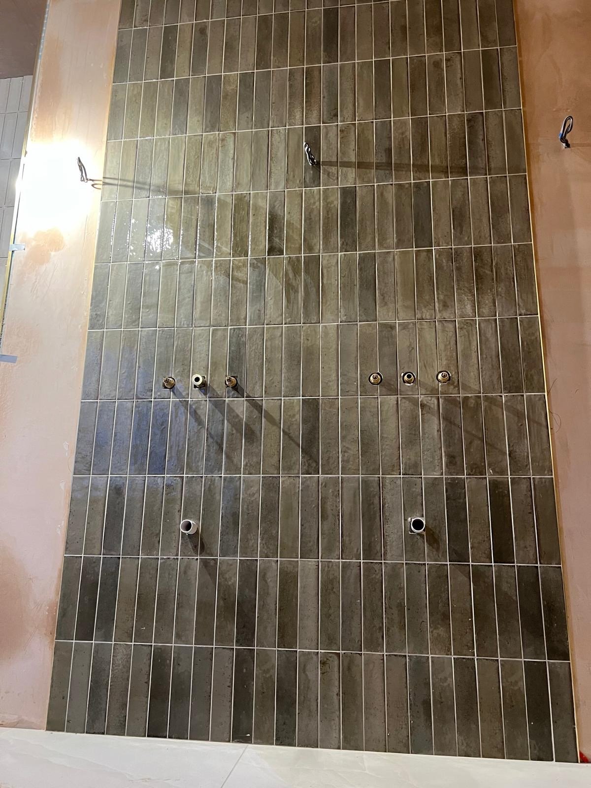 Under construction bathroom wall with green tiles and plumbing pipes, no fixtures installed yet.