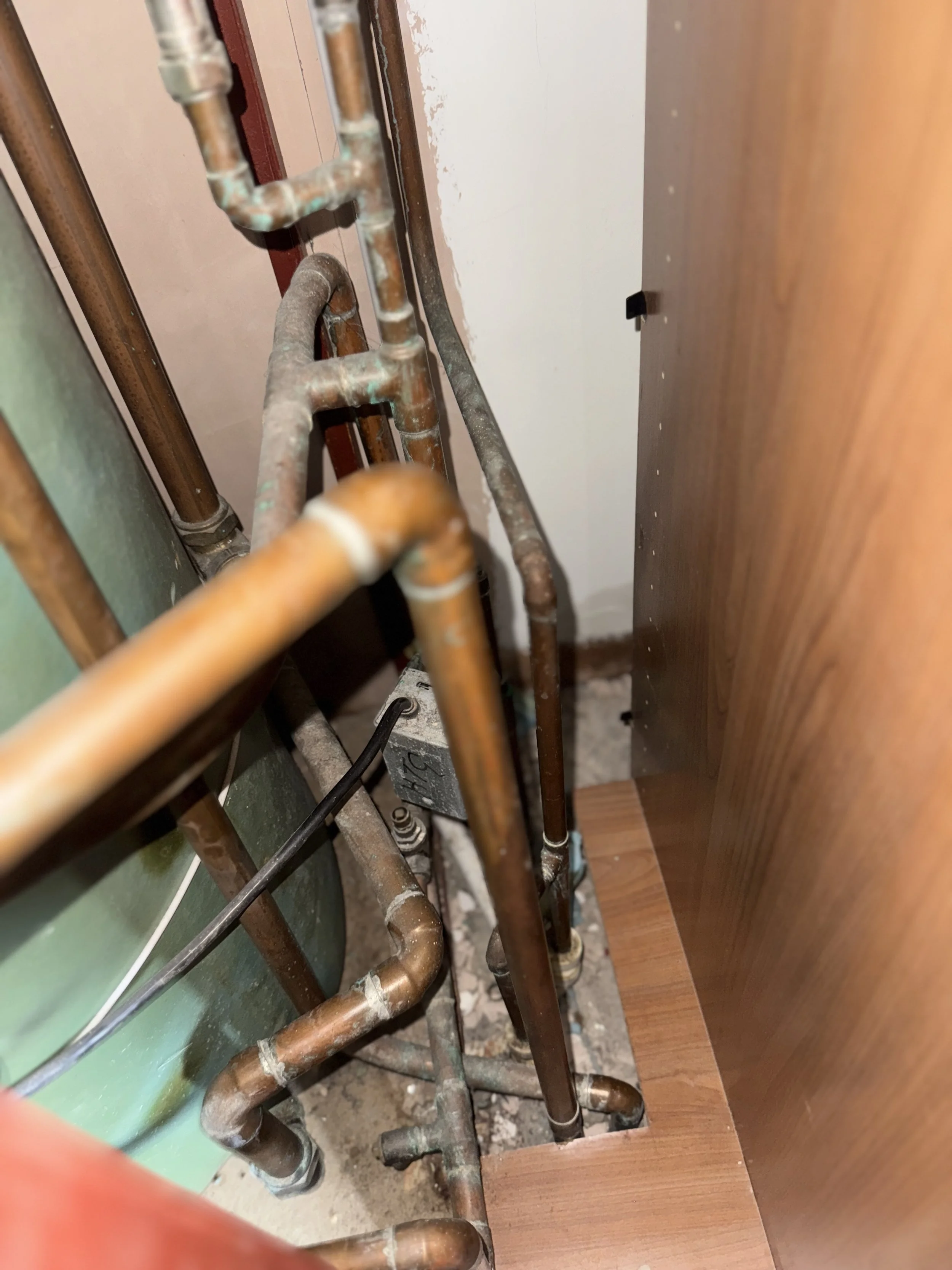 Close-up of copper plumbing pipes and fittings against a wall, in a construction or renovation setting.