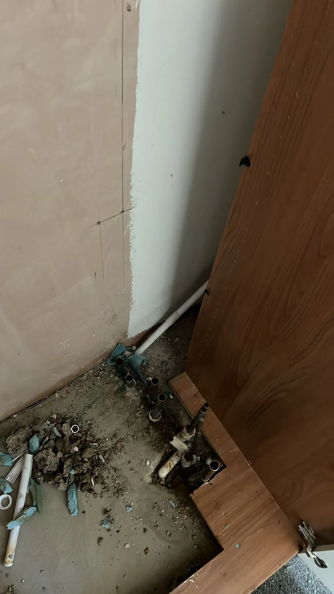 Part of a bathroom or laundry room under renovation showing plumbing pipes and a partially tiled wall.