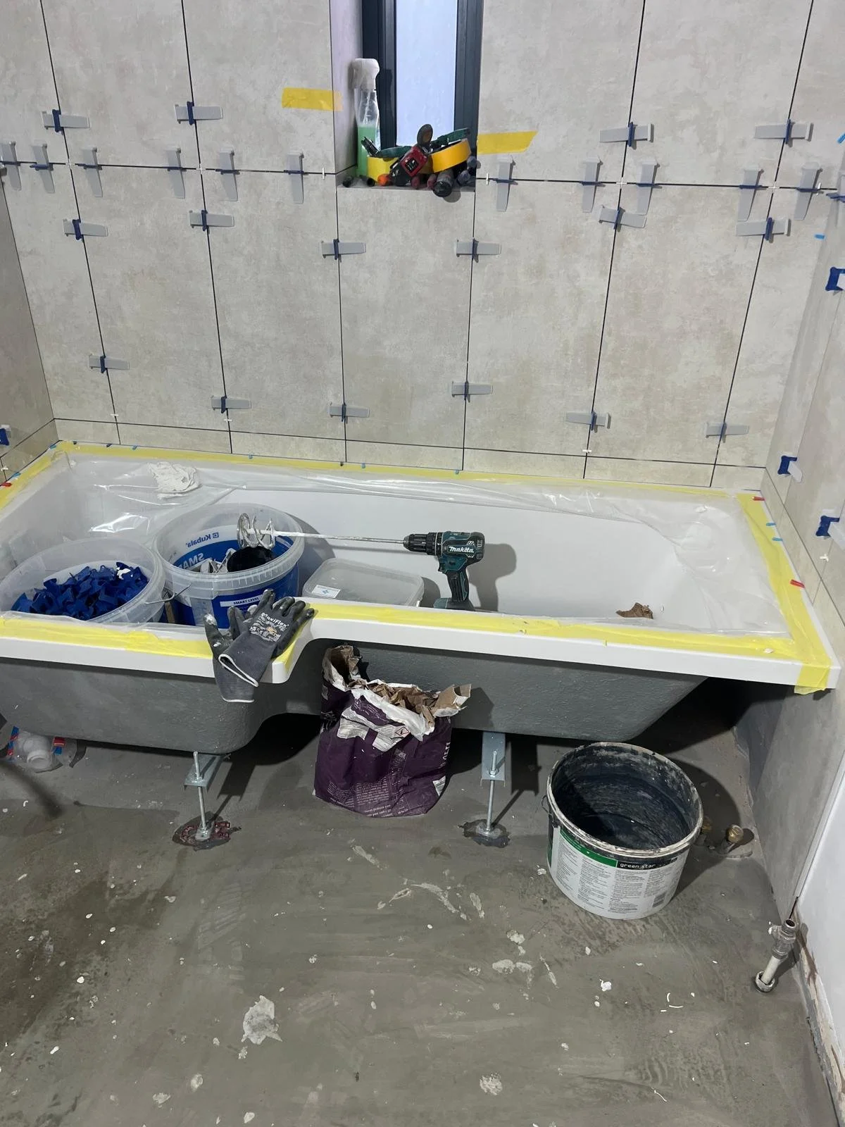 Bathroom under construction with a bathtub, tools, construction materials, and partially tiled walls.
