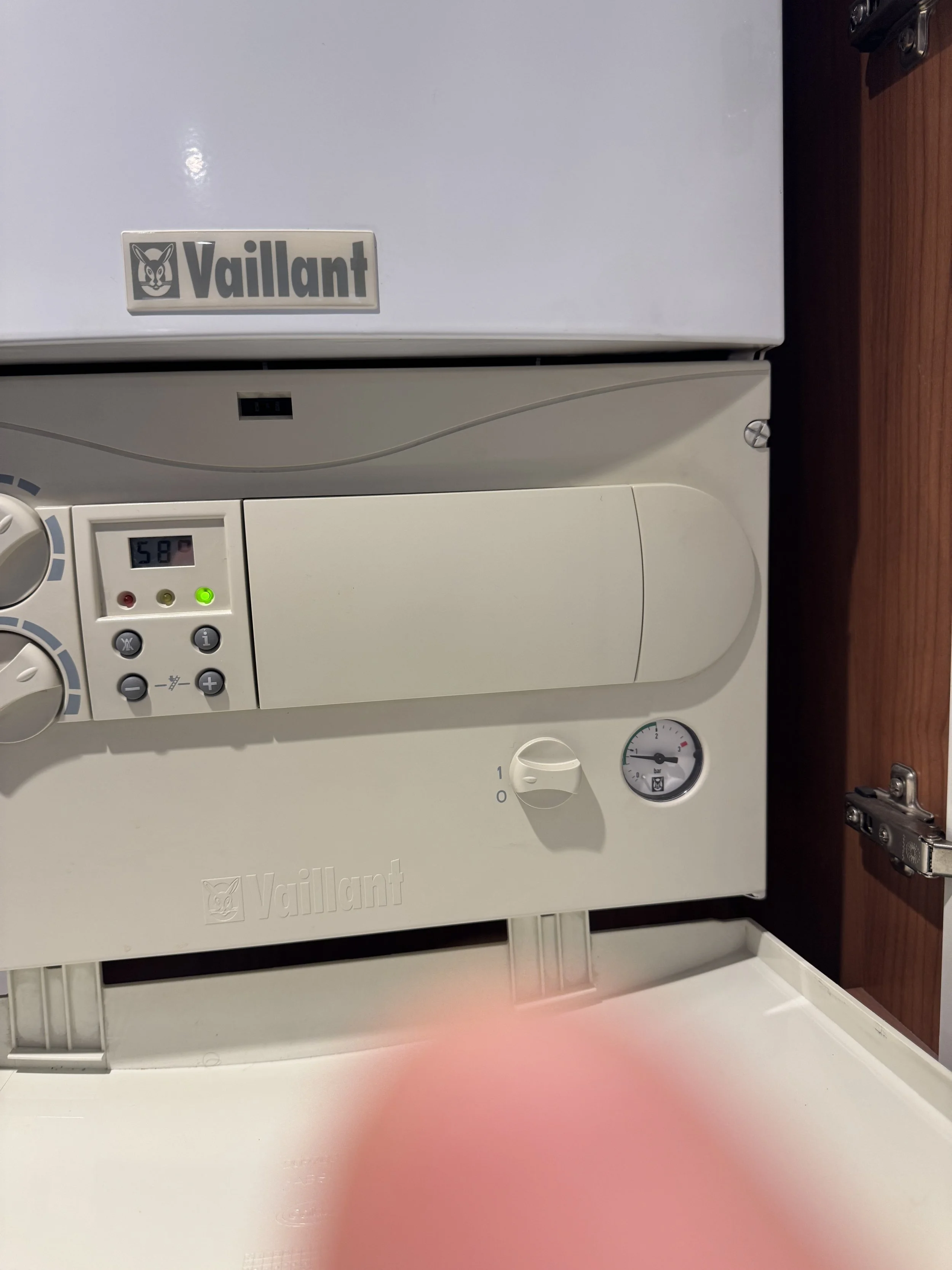A close-up of a Vaillant boiler mounted on a wall with a wooden panel nearby.