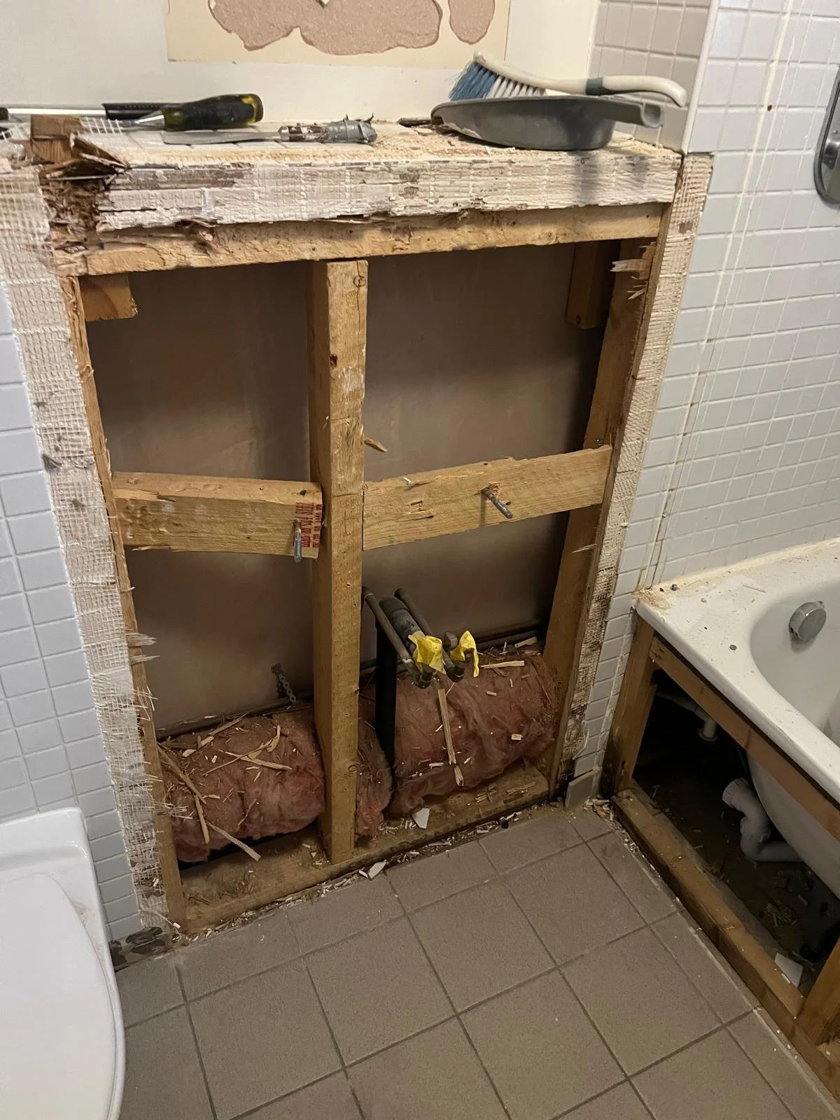 Bathroom vanity frame under construction with exposed wooden studs, insulation, and plumbing pipes; tools and materials on the countertop.