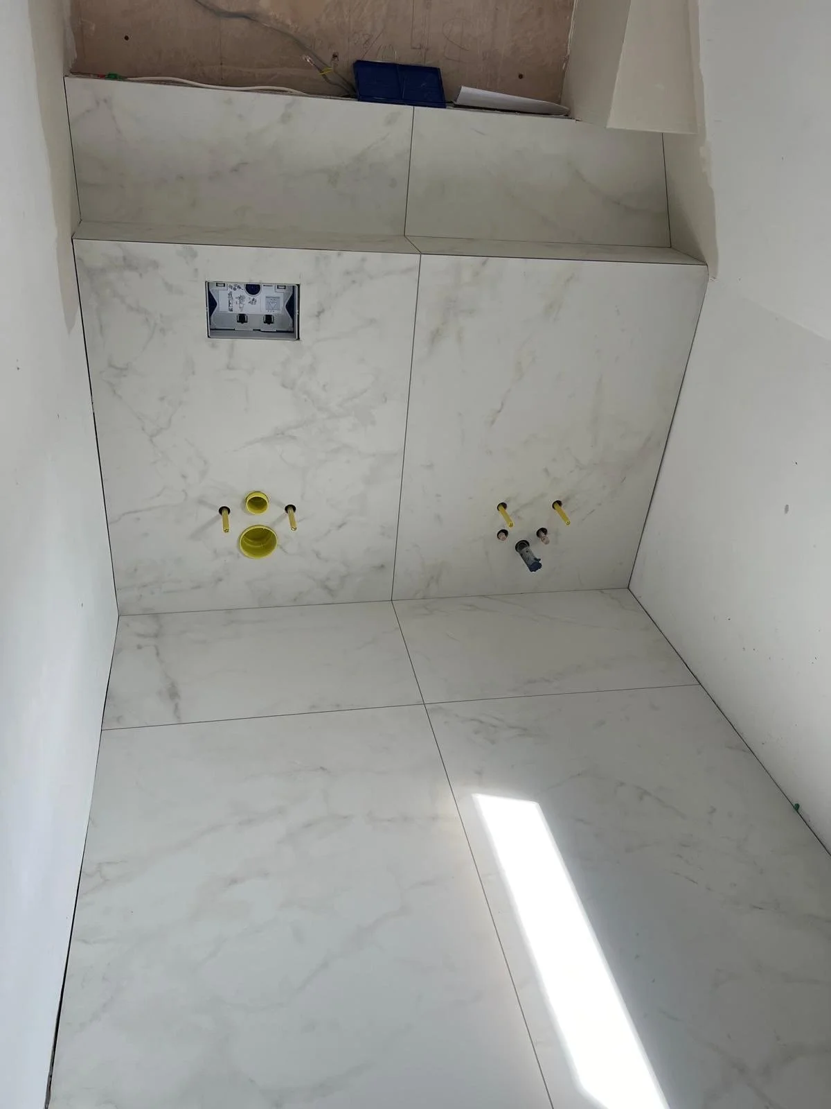 Construction site with marble tiling on walls and floor, with plumbing and electrical fixtures installed for a bathroom or kitchen area, but no appliances or fixtures are yet in place.
