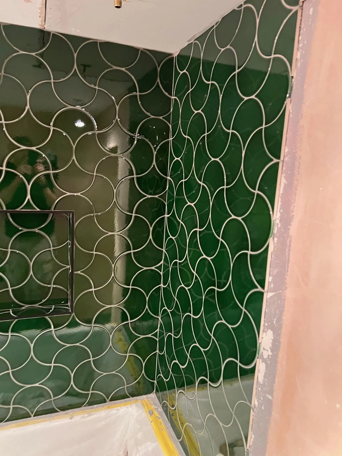 Interior of a room under construction with green tiled walls featuring a wavy pattern and a doorway frame.