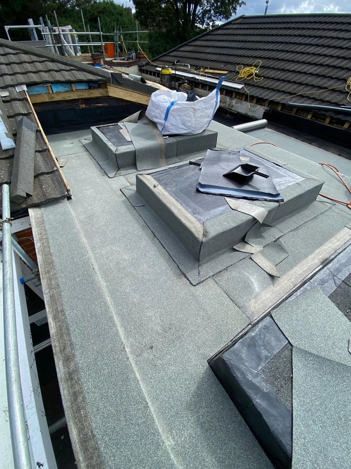 A roof under construction with multiple skylights and roofing materials, tools, and equipment visible.