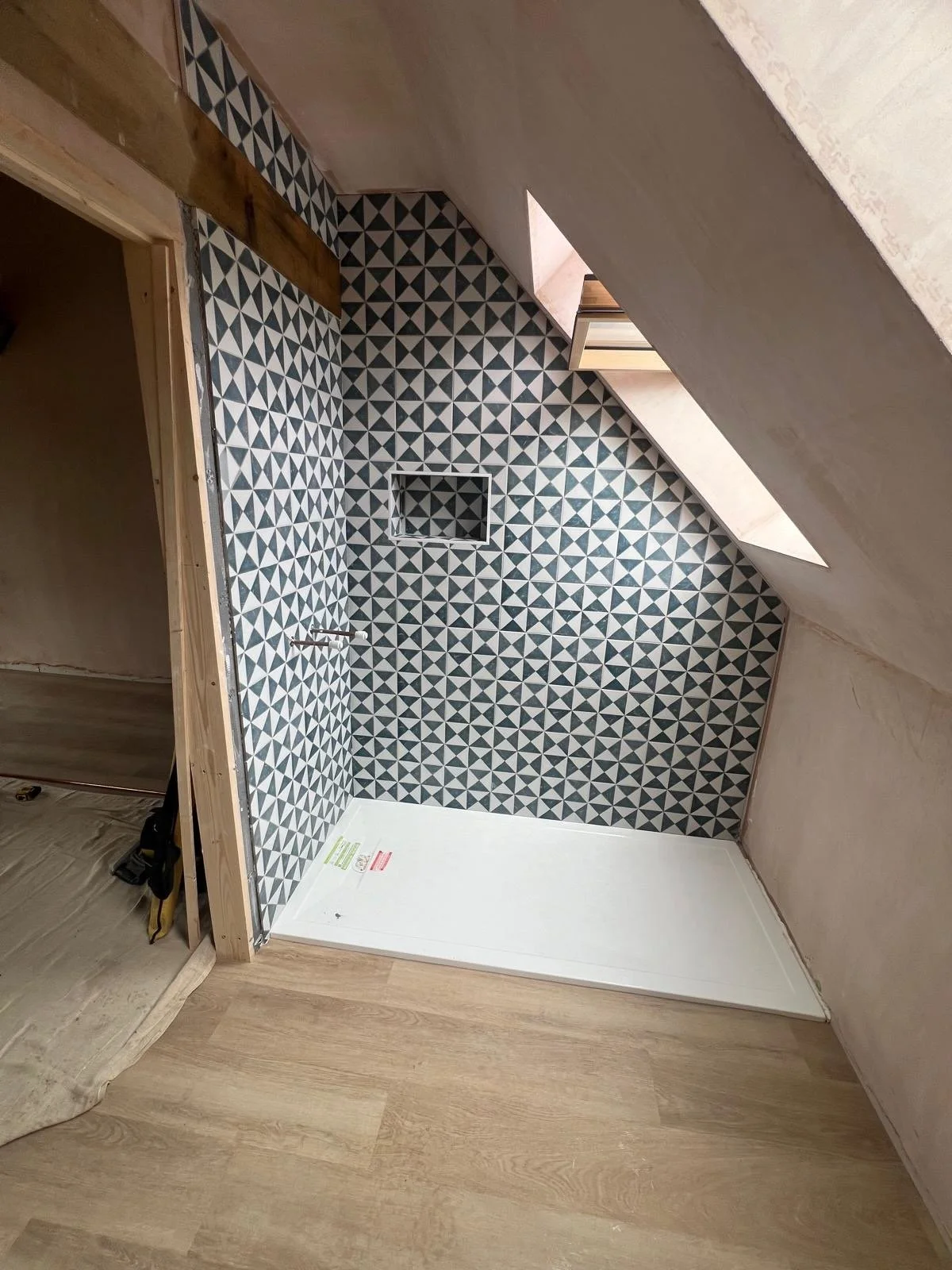 Interior of a room under construction with geometric black and white patterned wall tiles, a sloped ceiling with a skylight, and a white floor.