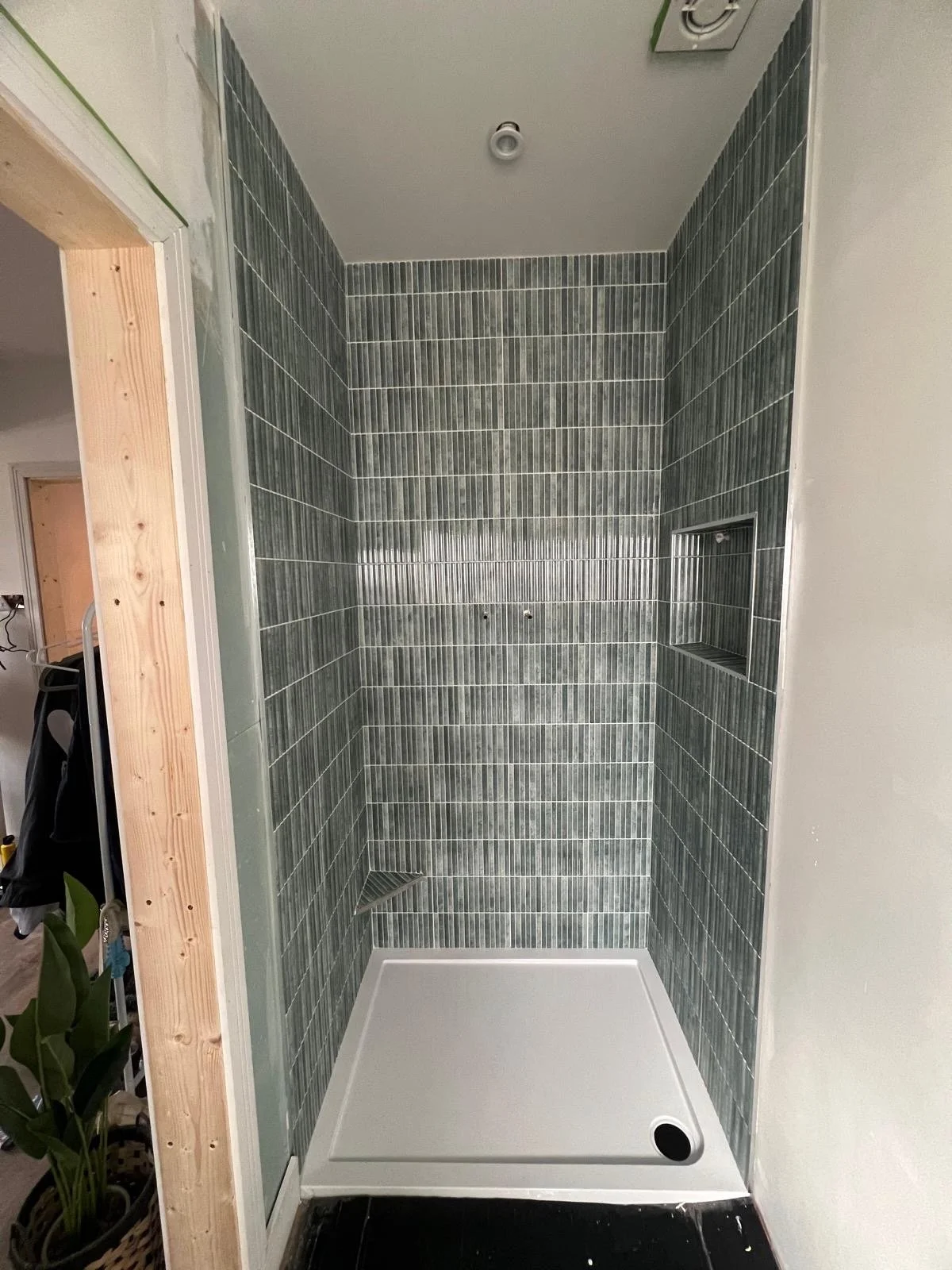 Empty walk-in shower with dark grey vertical tile walls, built-in niche, small drain, and a white shower base.