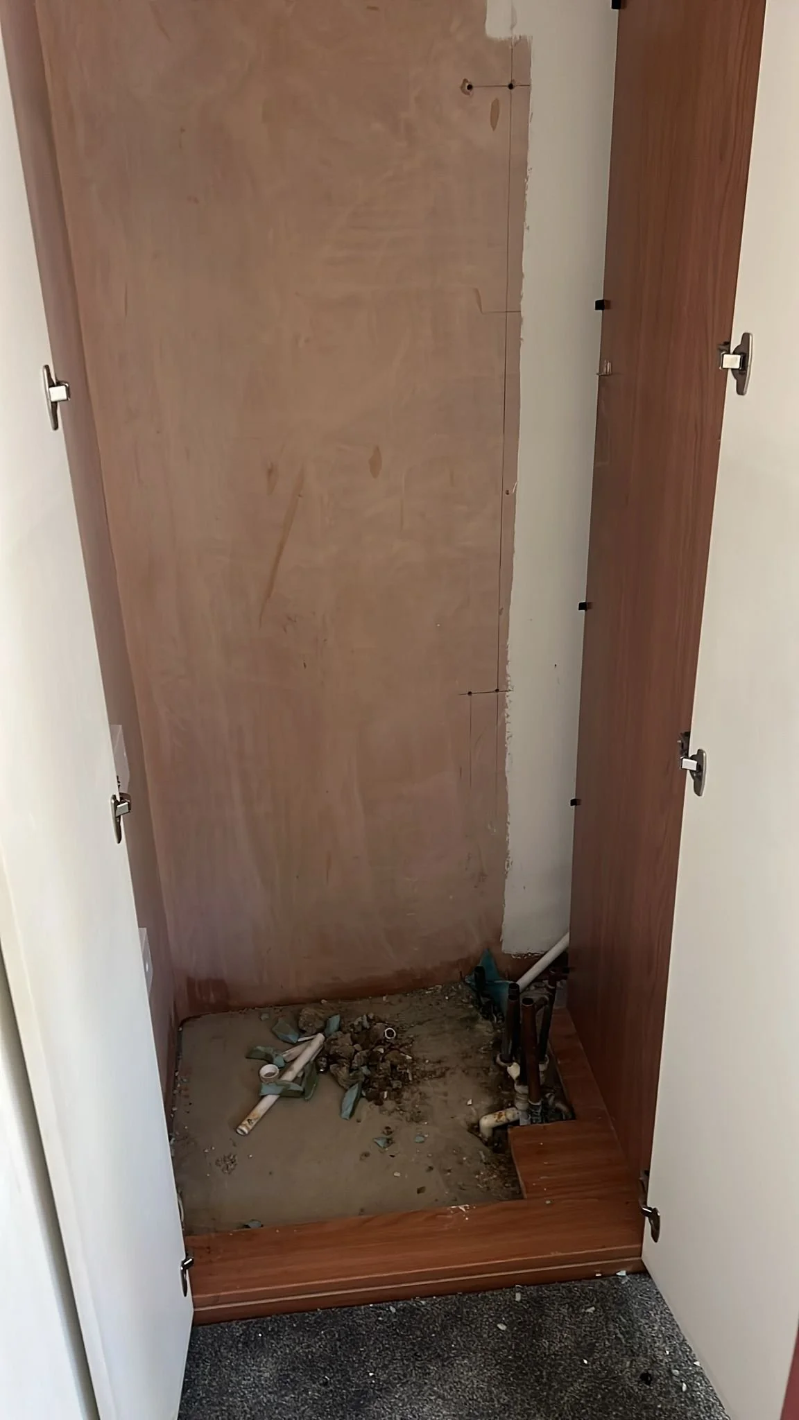 The cabinet doors are open, revealing an unfinished space with exposed plumbing and debris on the floor, indicating ongoing renovation or repair work.