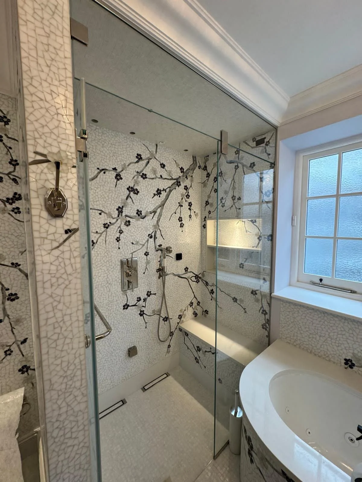 Modern bathroom with a glass-enclosed shower featuring floral mosaic tiles and a window with frosted glass.
