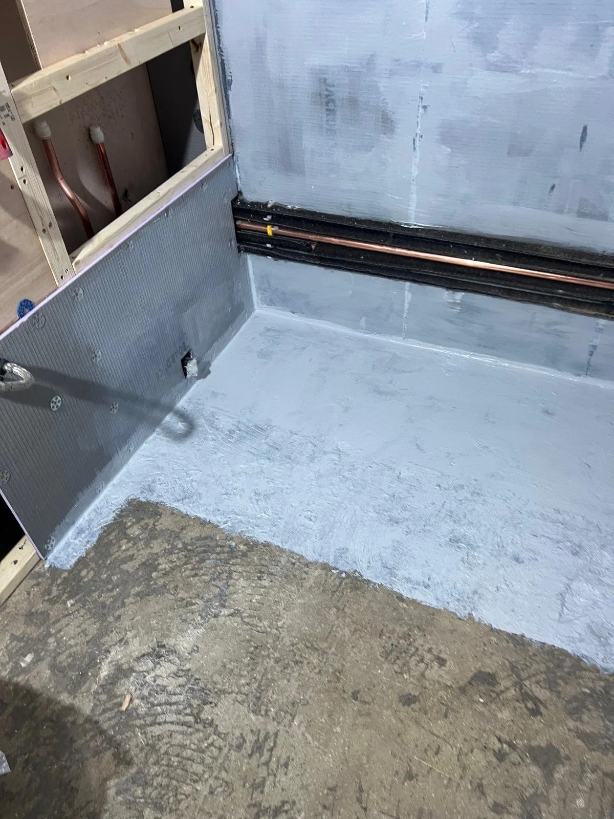Intersection of a gray concrete floor and a rougher dirt surface, with partially installed electrical wiring and plumbing in a building under construction.