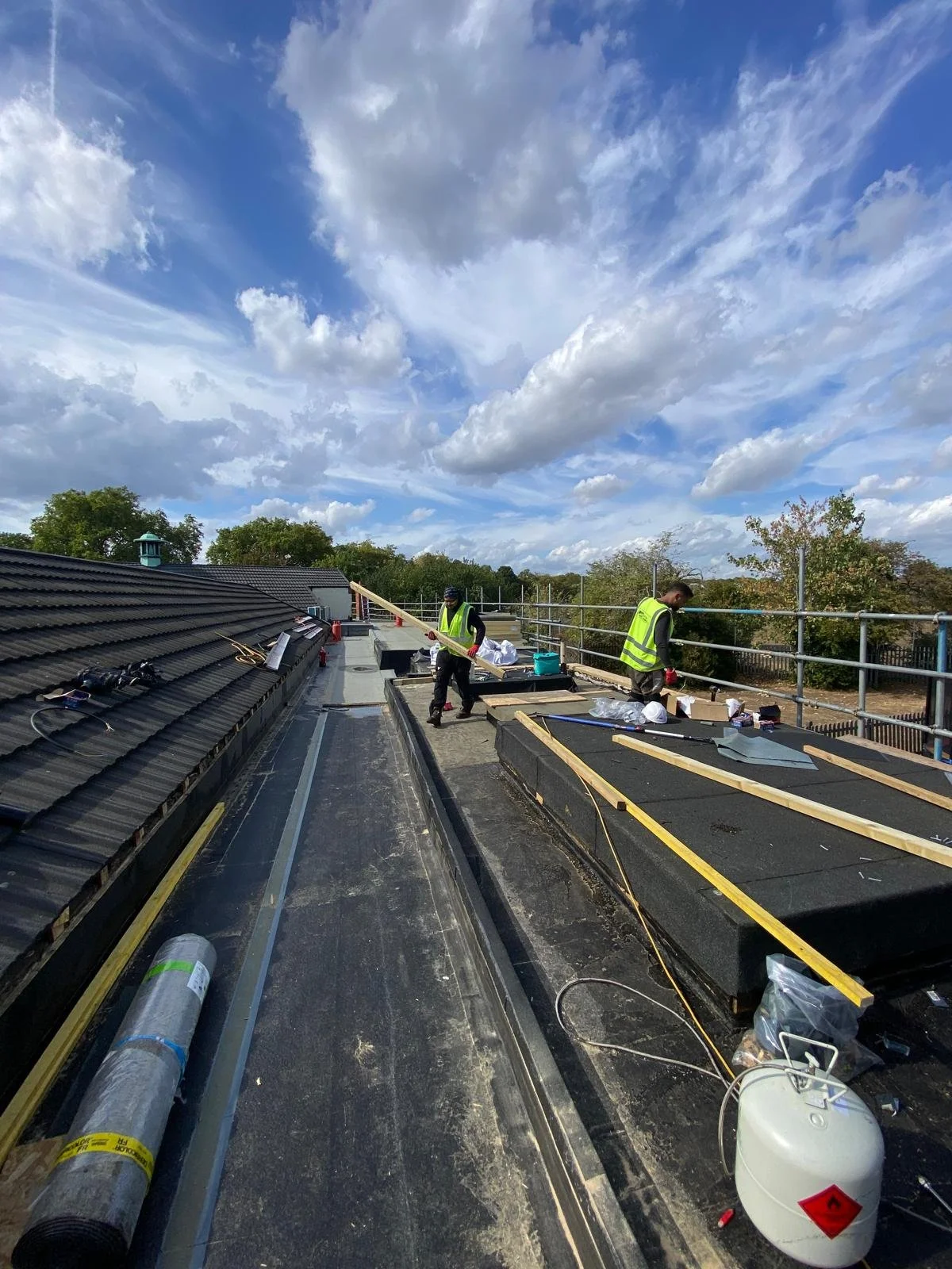 Construction workers installing roofing materials on a building during daytime, with a partly cloudy sky overhead.