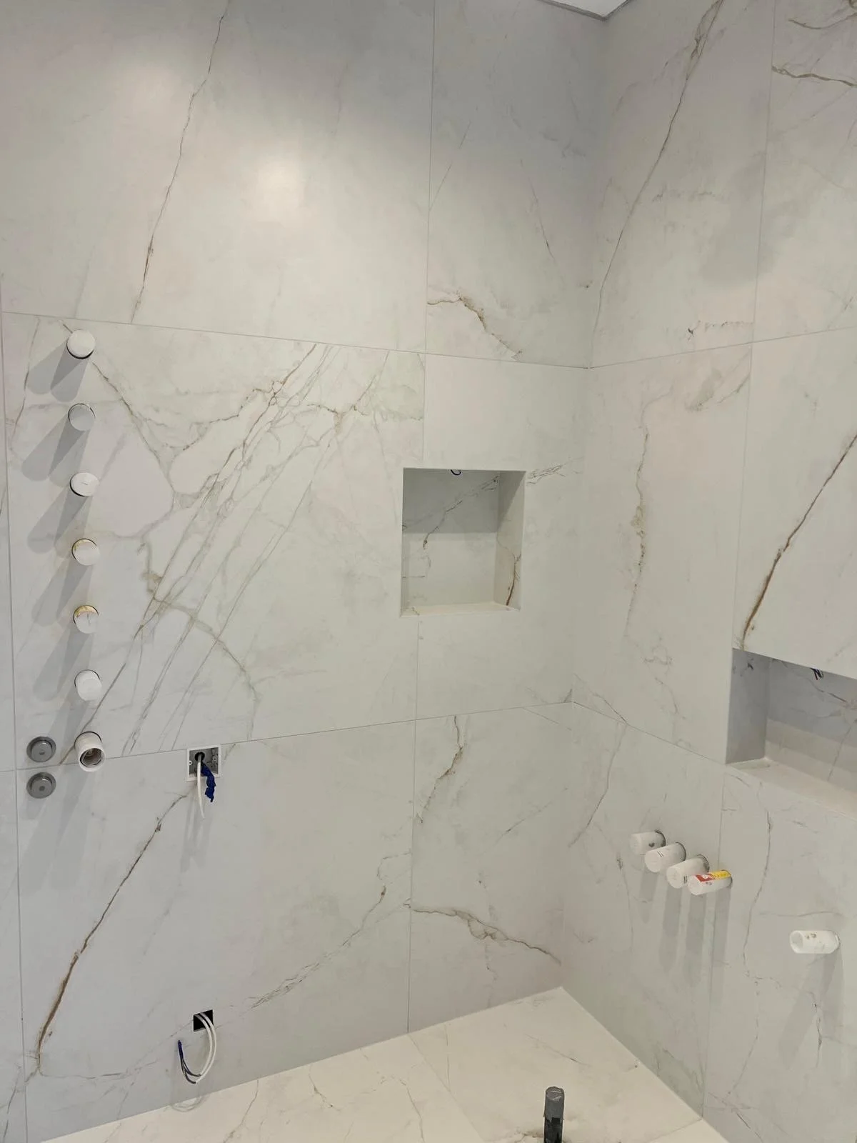 White marble tiled bathroom shower with built-in niches and multiple plumbing fixtures