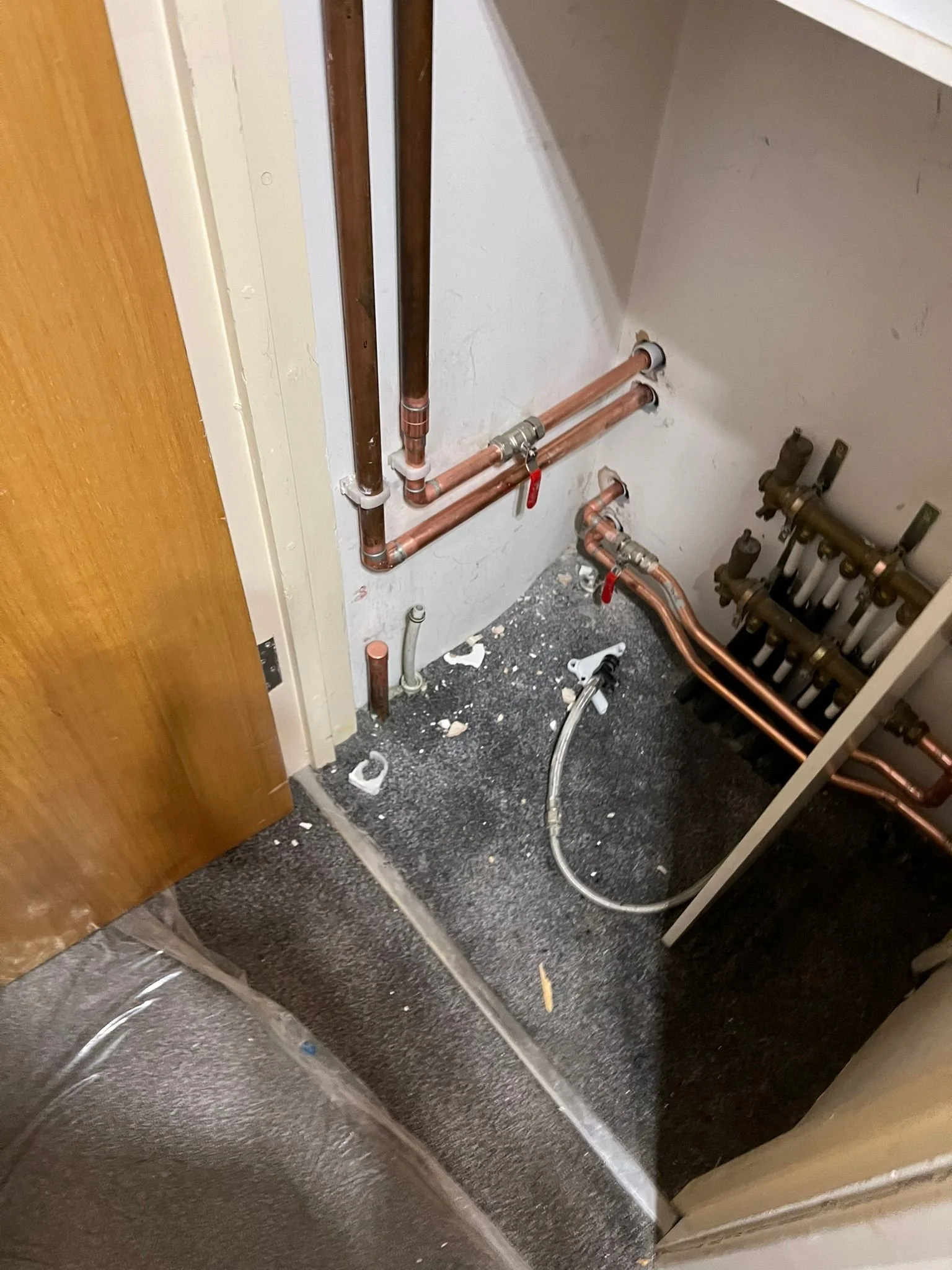 Close-up view of plumbing pipes and fittings inside a wall cavity, with a partially visible floor and door on the left.