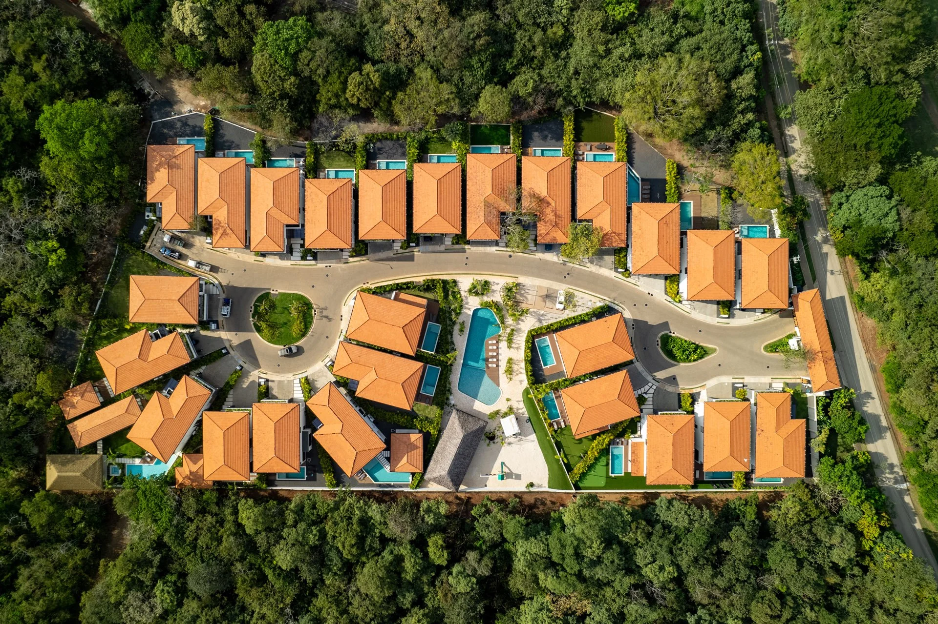 Aerial view of a residential complex with orange-tiled roofs, landscaped courtyards, a swimming pool, and surrounded by greenery.