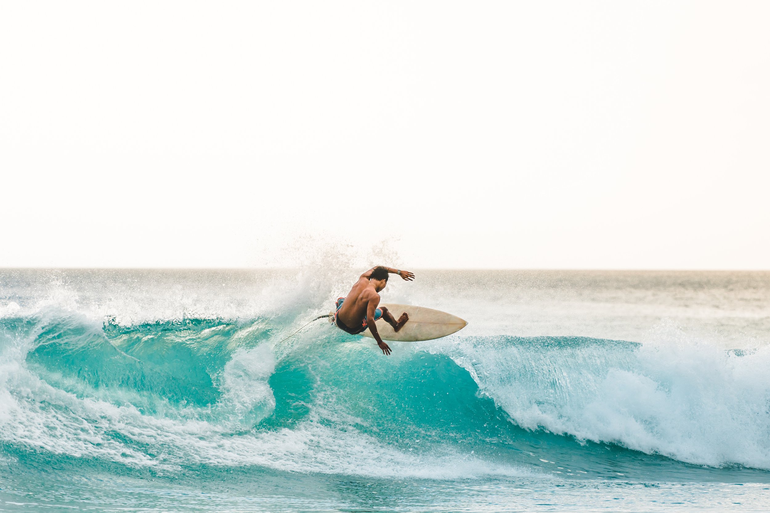 A male surfer riding a blue wave on a surfboard in the ocean.