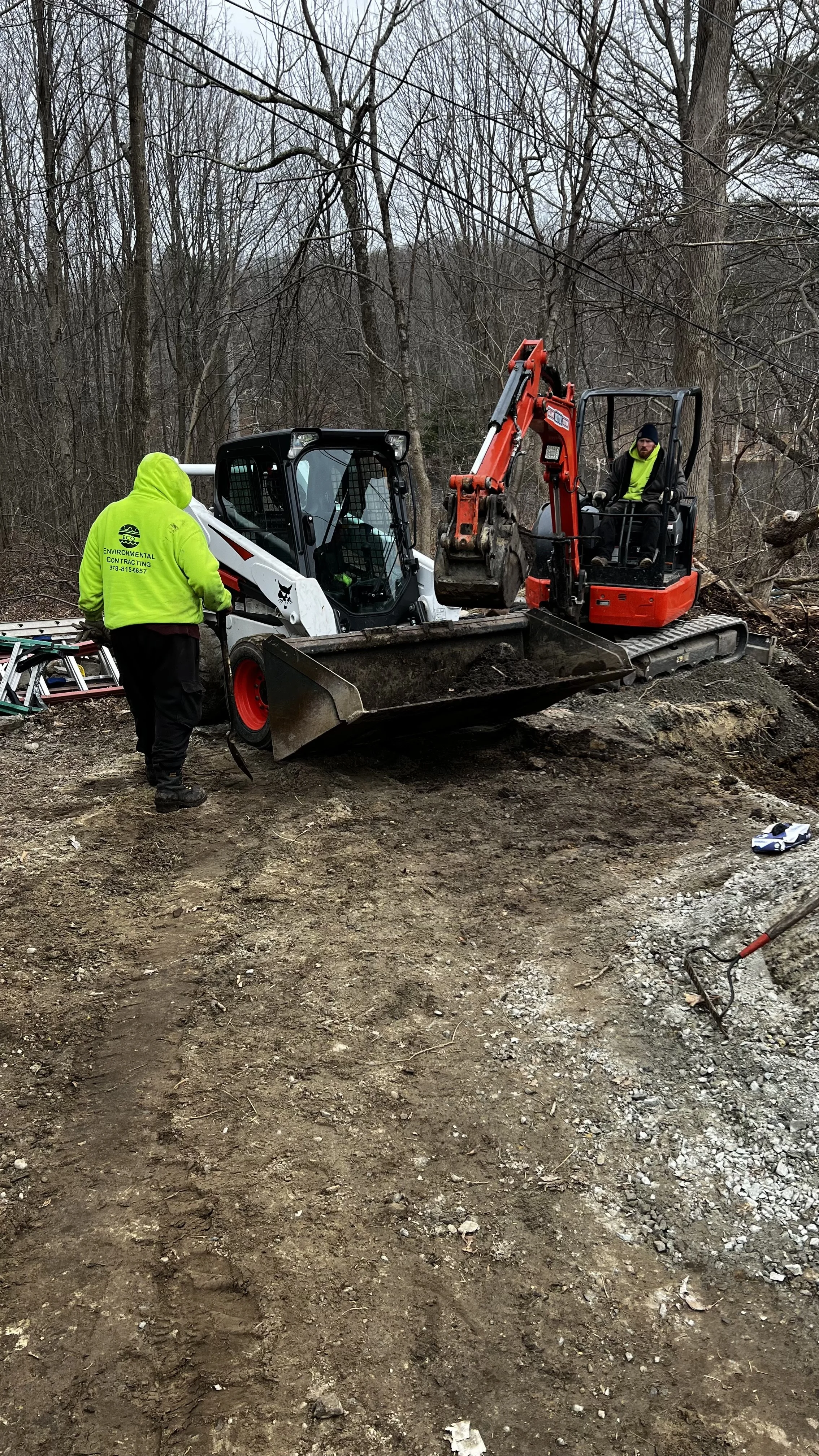 transferring contaminated soil from excavator to bobcat to stock pile