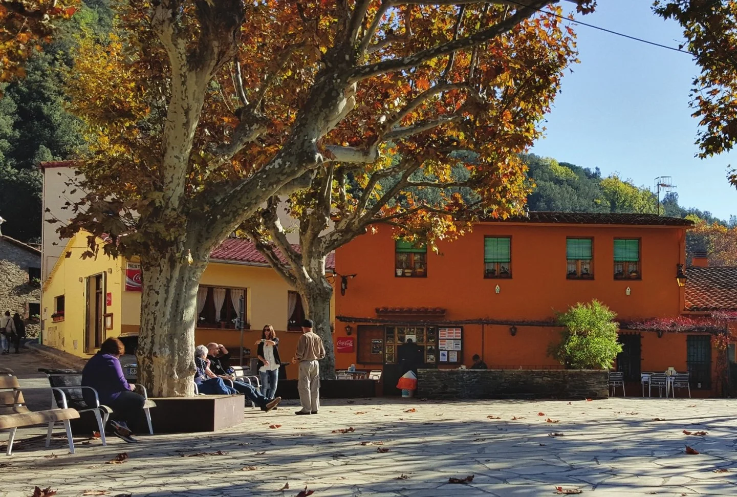 La plaça de la Vila de Montseny con terrazas, fachadas cálidas y hojas de otoño