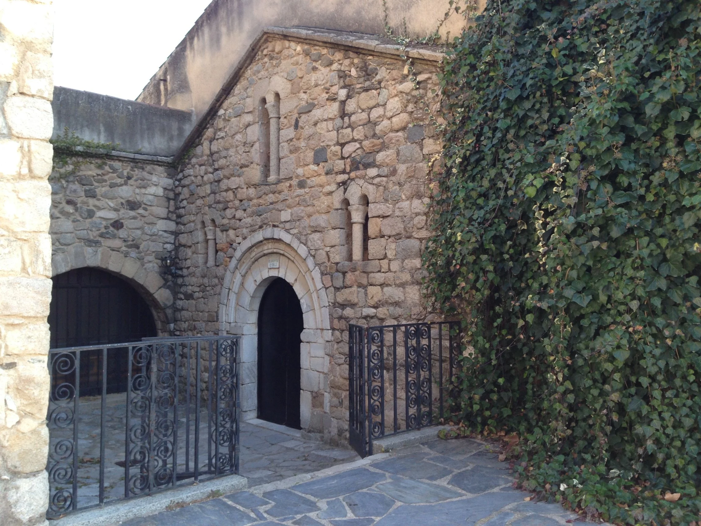 Fachada románica de Sant Vicenç de Gualba, con puerta de arco de piedra y hiedra junto al acceso
