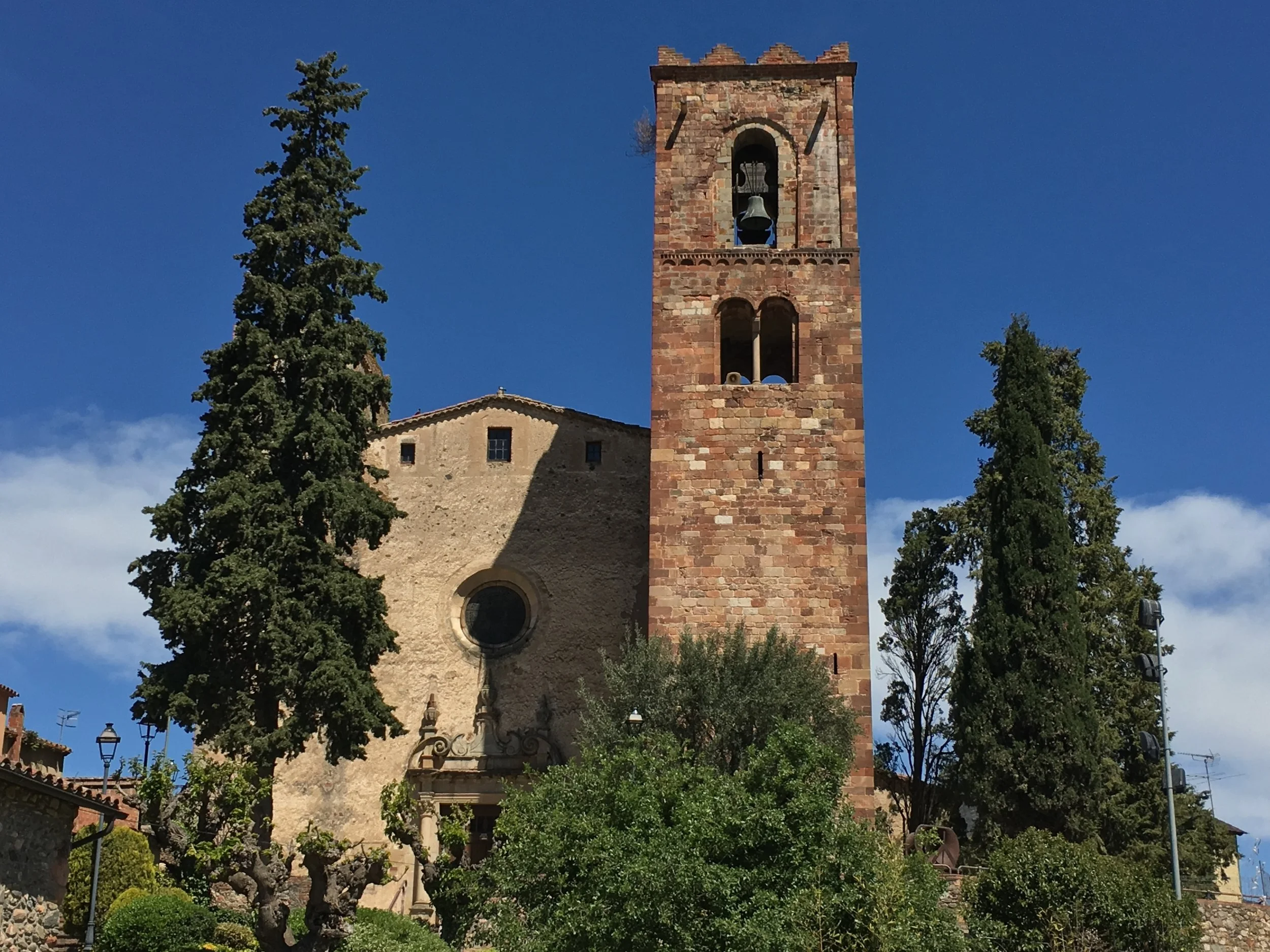Iglesia de Sant Pere de Vilamajor y Torre Roja entre árboles, con cielo azul