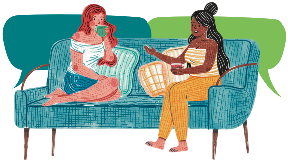 Two women sitting on a blue couch having a conversation. One woman with red hair is drinking from a green mug, and the other woman with black hair is holding a red mug and gesturing with her hand.
