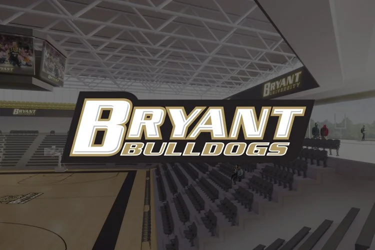 An indoor basketball arena with seating and a large display screen showing the text 'Bryant Bulldogs'.