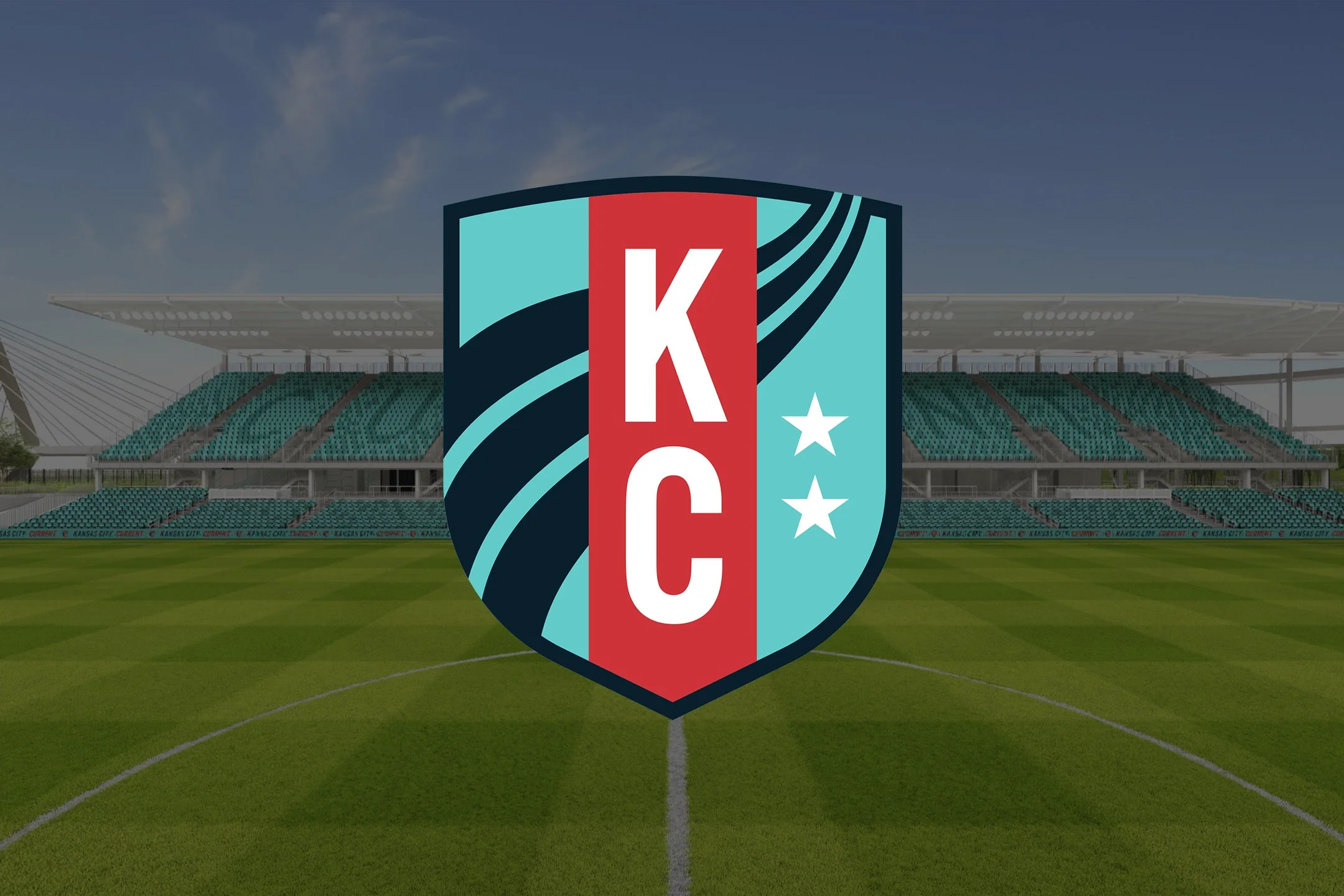 A sports stadium with green seating and an empty field, featuring a large Kansas City Chiefs logo on the field, with the sky in the background.