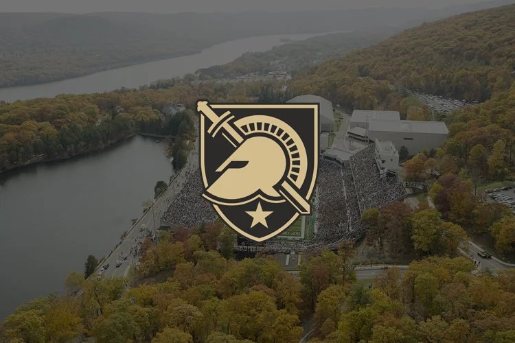 Aerial view of a football stadium surrounded by trees and a river, with a military emblem overlay