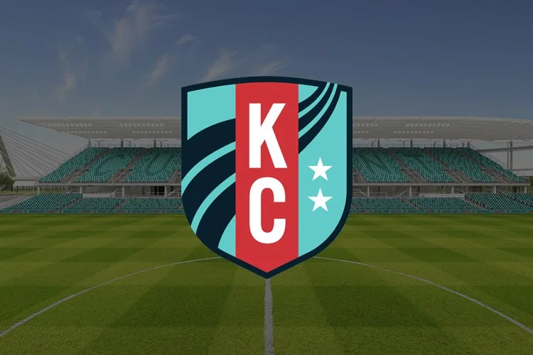 Vista del campo de fútbol en un estadio con el logotipo del Sporting Kansas City en el centro de la imagen, con gradas y estructura del estadio en el fondo.