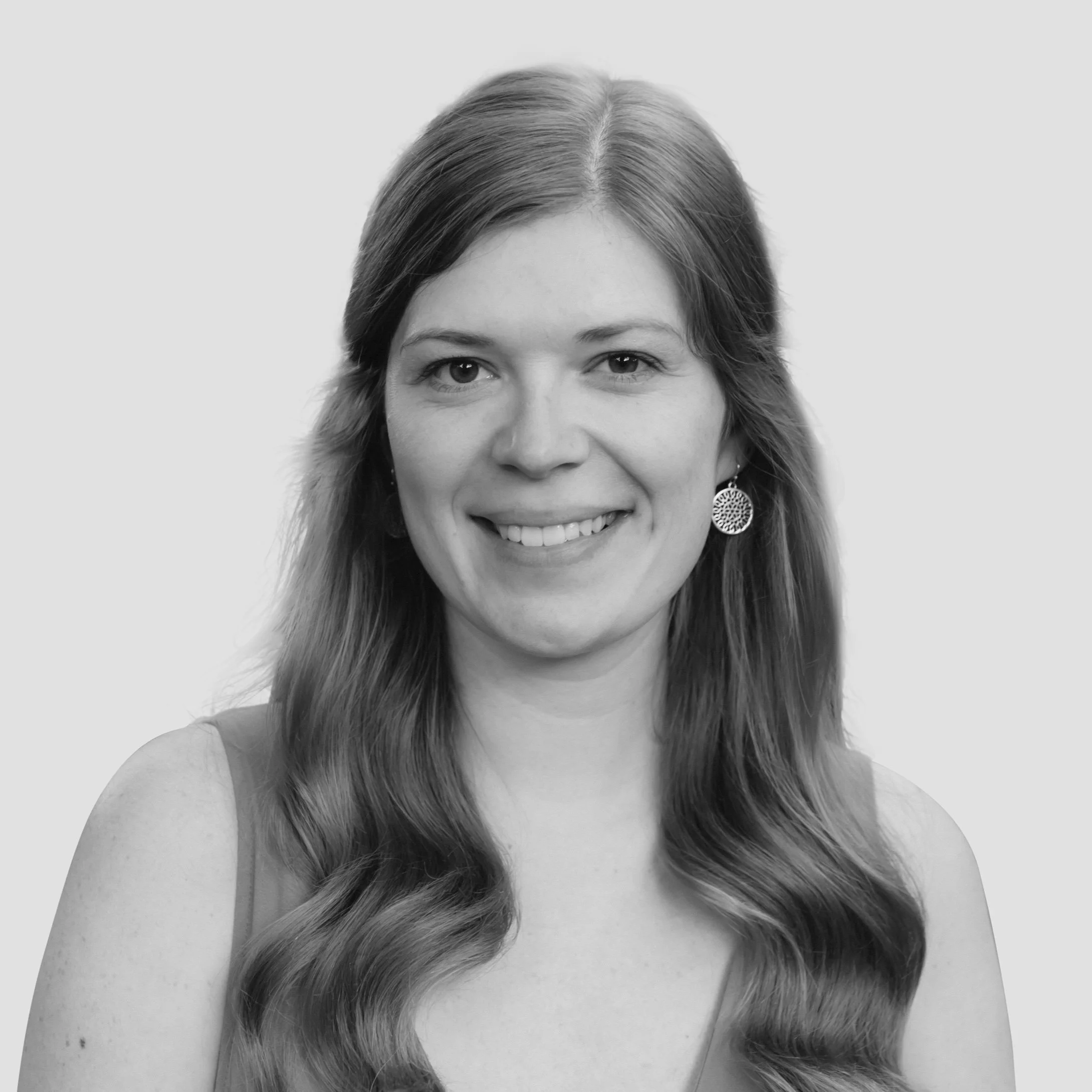 Close-up black-and-white photo of a woman with long hair, smiling, wearing a decorative earring, against a plain light background.