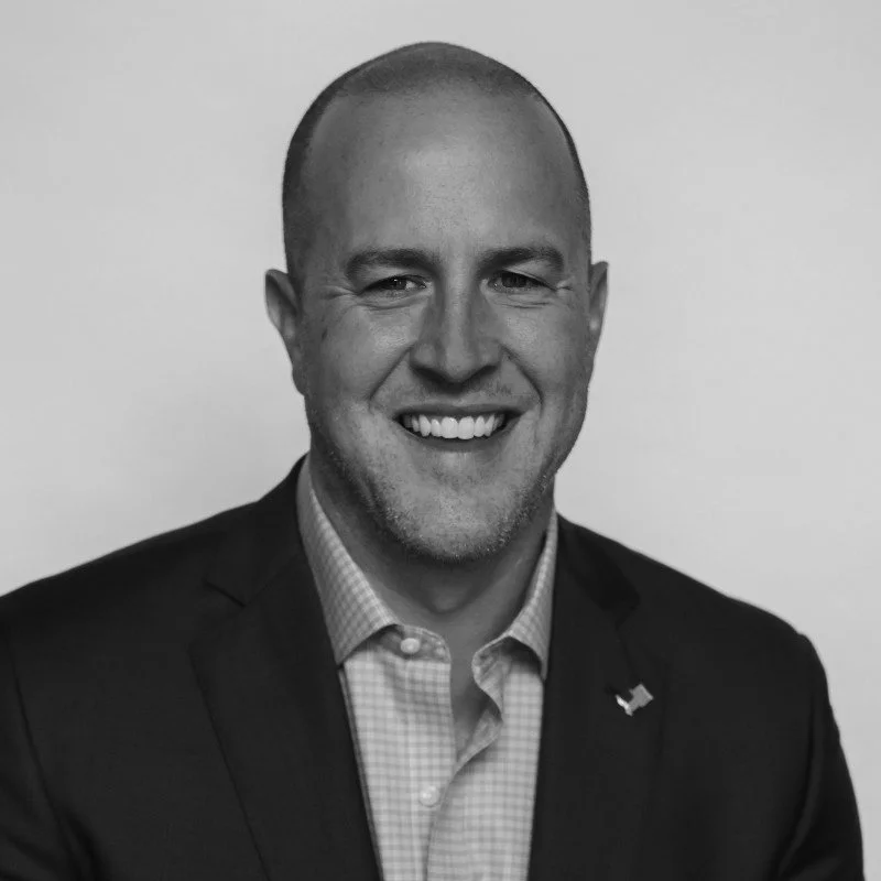 Black and white portrait of a smiling man wearing a suit and checkered shirt