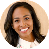 A smiling woman with long dark hair, wearing a white top, in front of a neutral background.