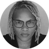 Black woman with glasses and light-colored dreadlocks, looking at the camera