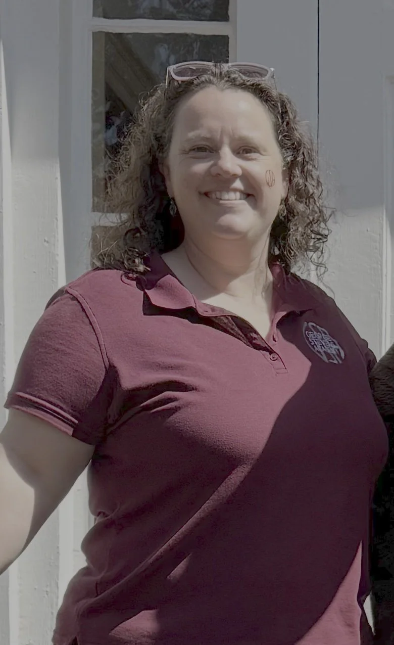 A woman with curly hair wearing a purple scarf and earrings outdoors.