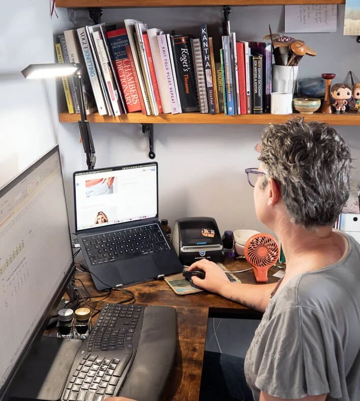Rachael Prest working at a dual-screen setup with books and design software.
