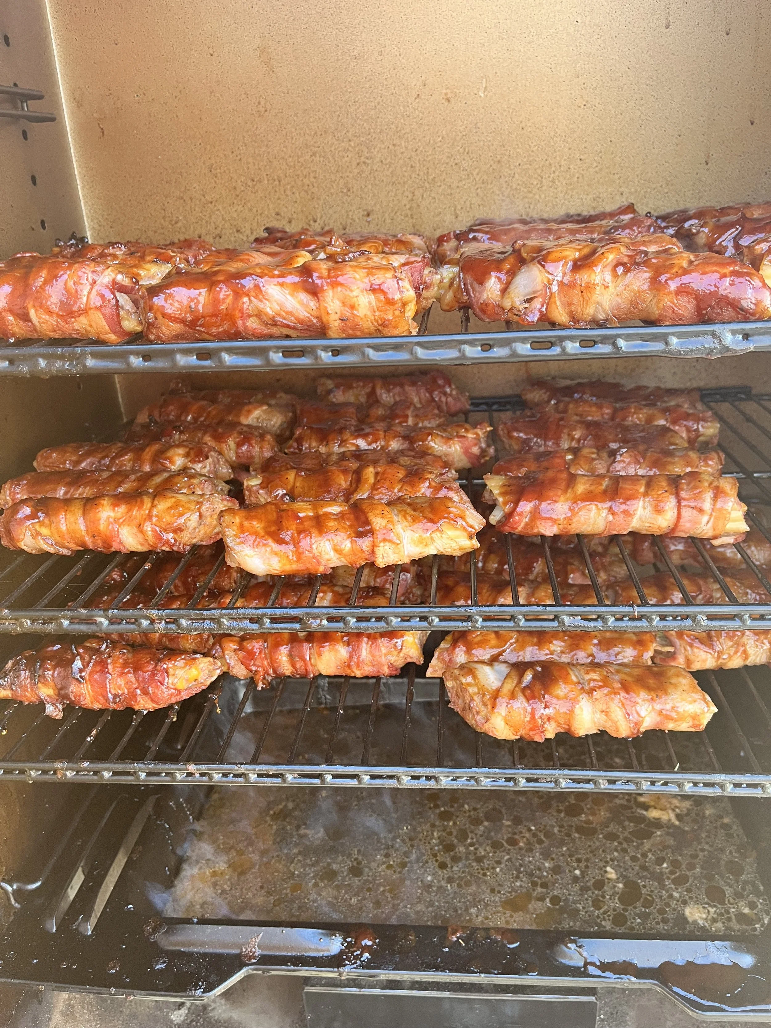 Meat ribs with barbecue sauce on metal racks inside an oven or smoker.