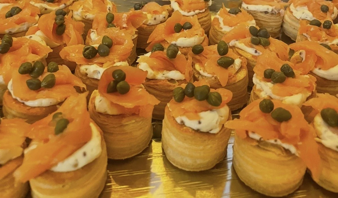 Multiple puff pastry appetizers topped with whipped cream, smoked salmon, and capers.