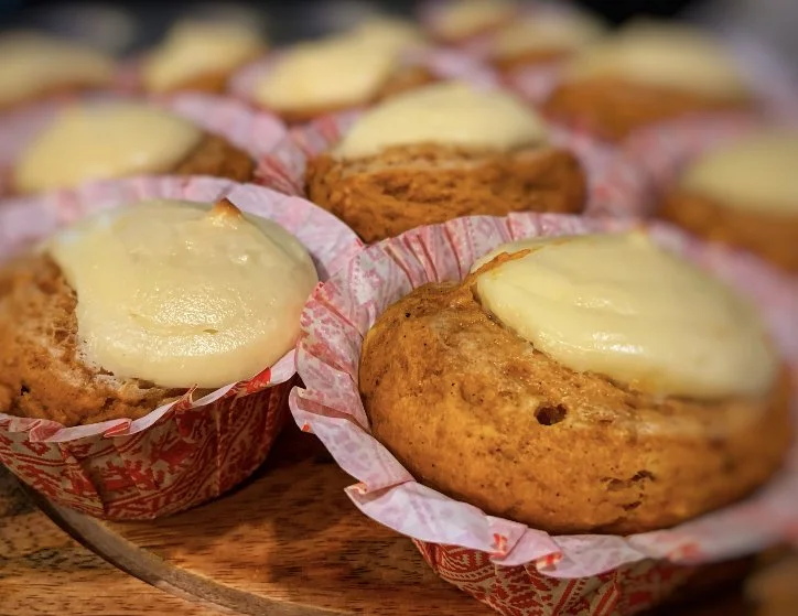 Close-up of muffins with melted cheese on top, in red patterned paper cups on a wooden surface.