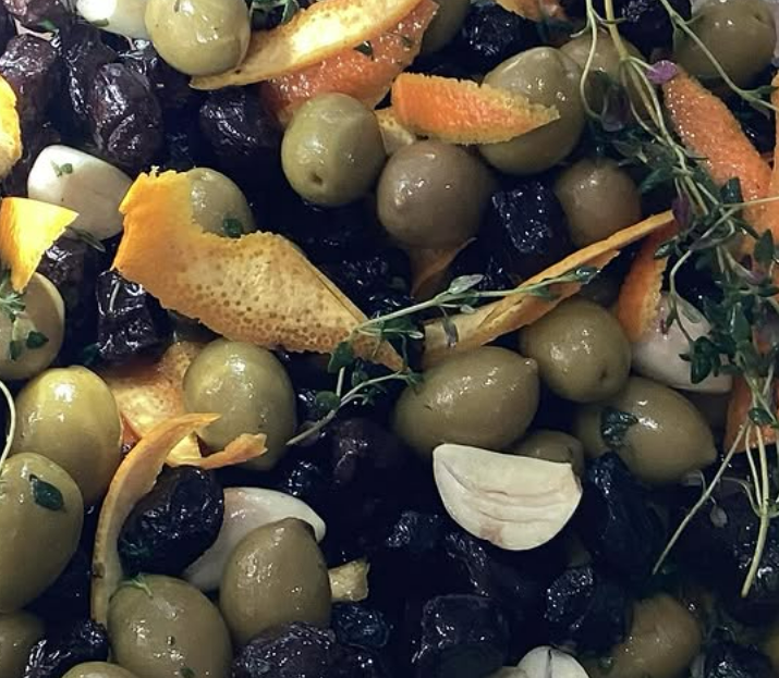 Close-up of a mixed salad with green olives, black olives, lemon peel, garlic, and herbs.
