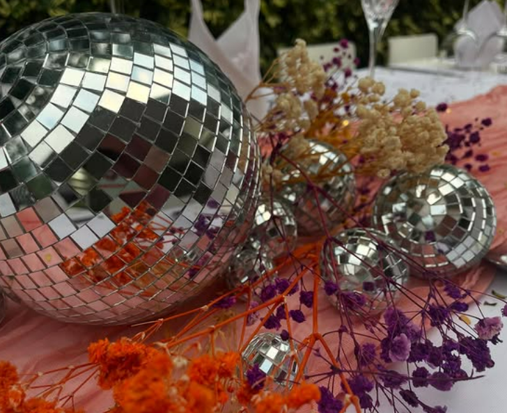 Decorative silver disco balls arranged on a table with colorful flowers and pink tablecloth at a party or celebration.