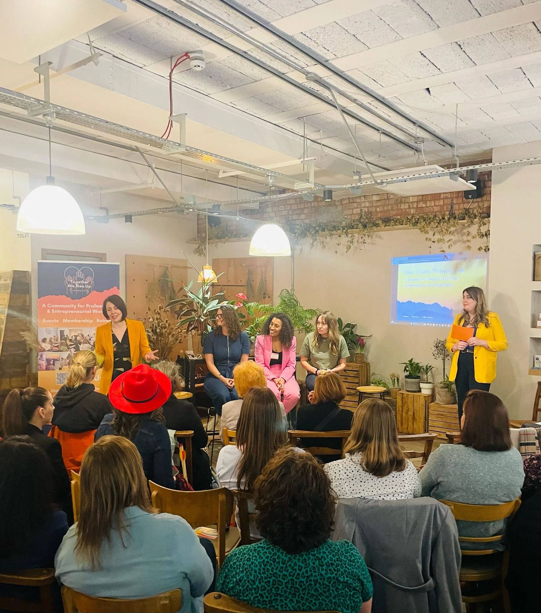 Panel of ladies with colourful clothes on speaking at an event guests looking at the speakers