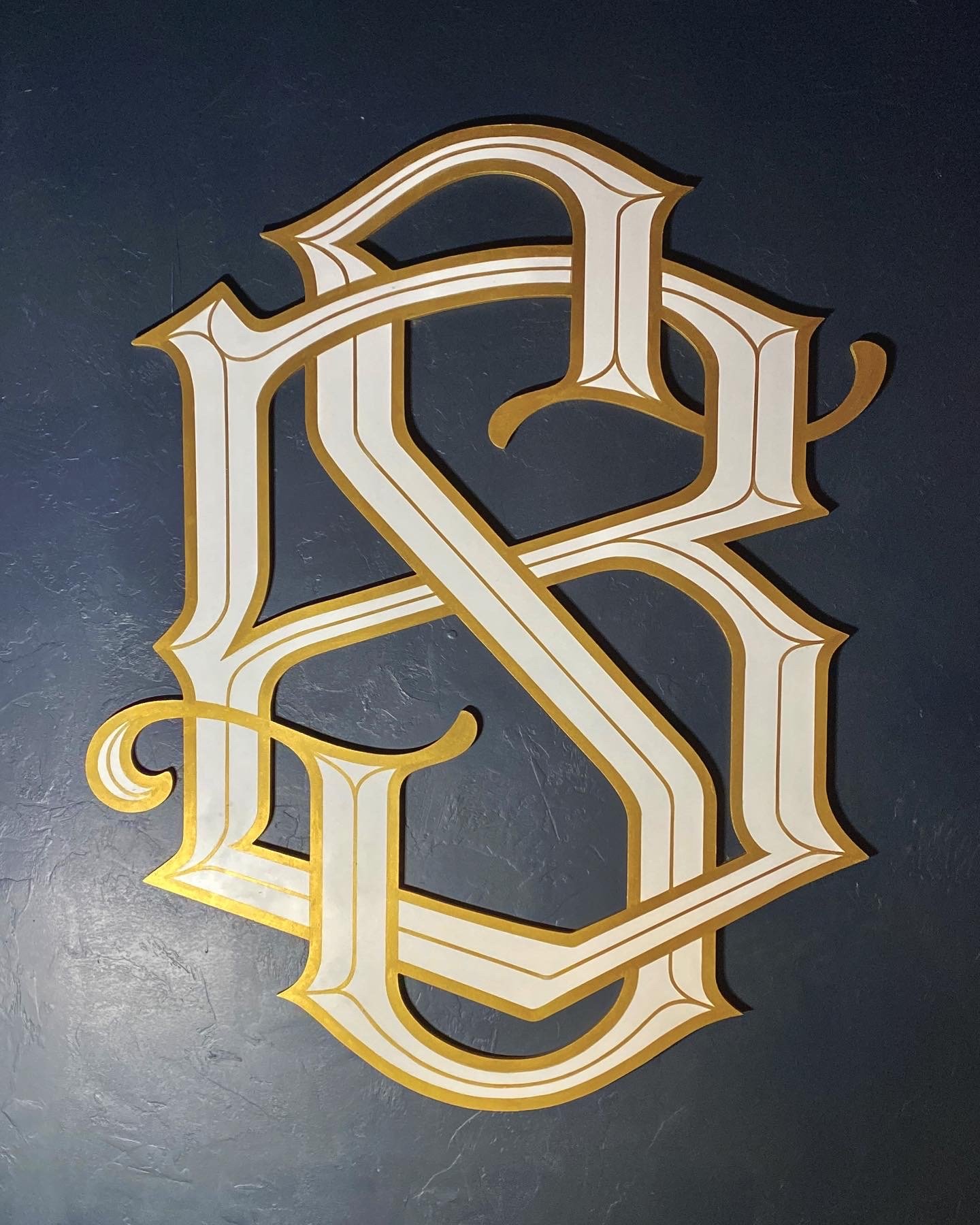 Decorative gold and white monogram letter R on dark background.