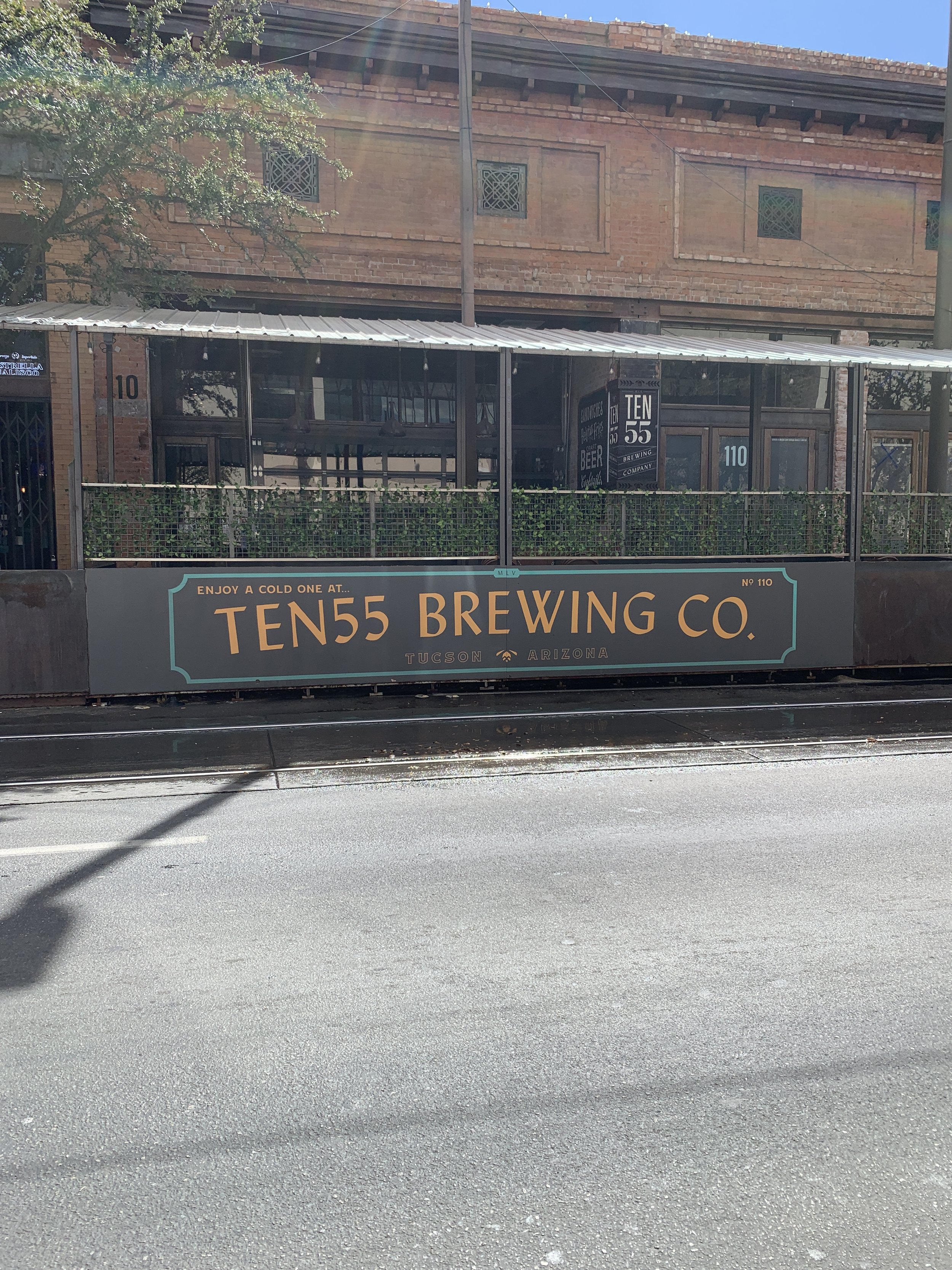 Sign for Ten55 Brewing Co. in Tucson, Arizona, advertising cold beer, mounted on a wall at a brewery with outdoor seating and an enclosed patio.